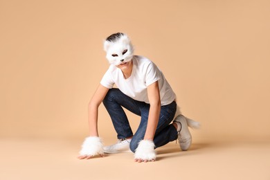 Photo of Quadrobics. Boy wearing cat mask, gloves and tail on beige background