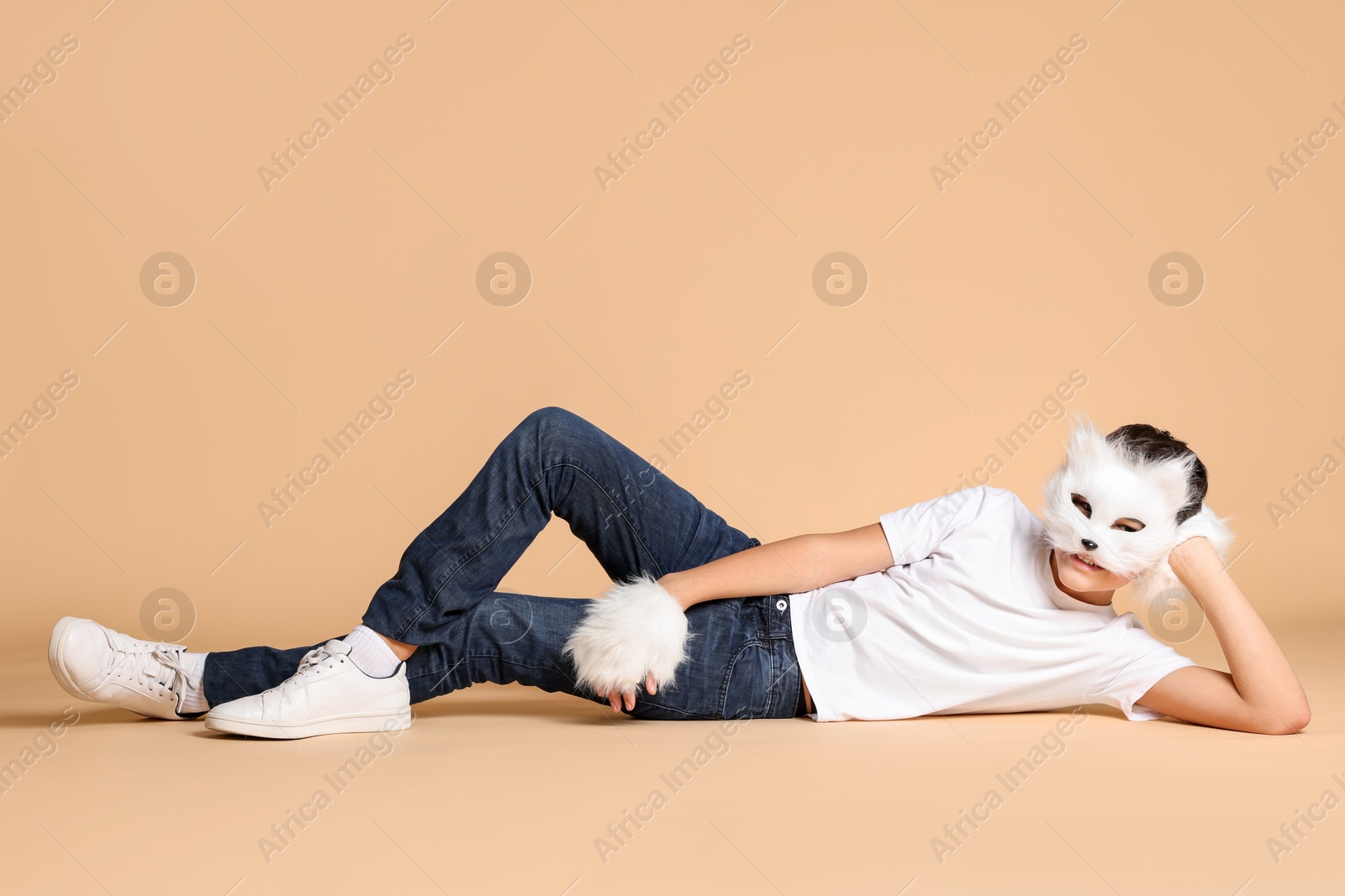 Photo of Quadrobics. Boy wearing cat mask and gloves on beige background