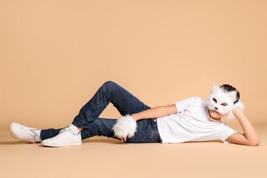 Photo of Quadrobics. Boy wearing cat mask and gloves on beige background