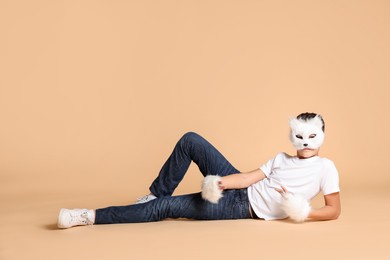 Photo of Quadrobics. Boy wearing cat mask and gloves on beige background