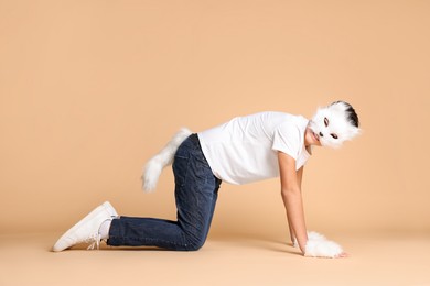 Photo of Quadrobics. Boy wearing cat mask, gloves and tail on beige background