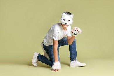 Photo of Quadrobics. Boy wearing cat mask, gloves and tail on pale olive background