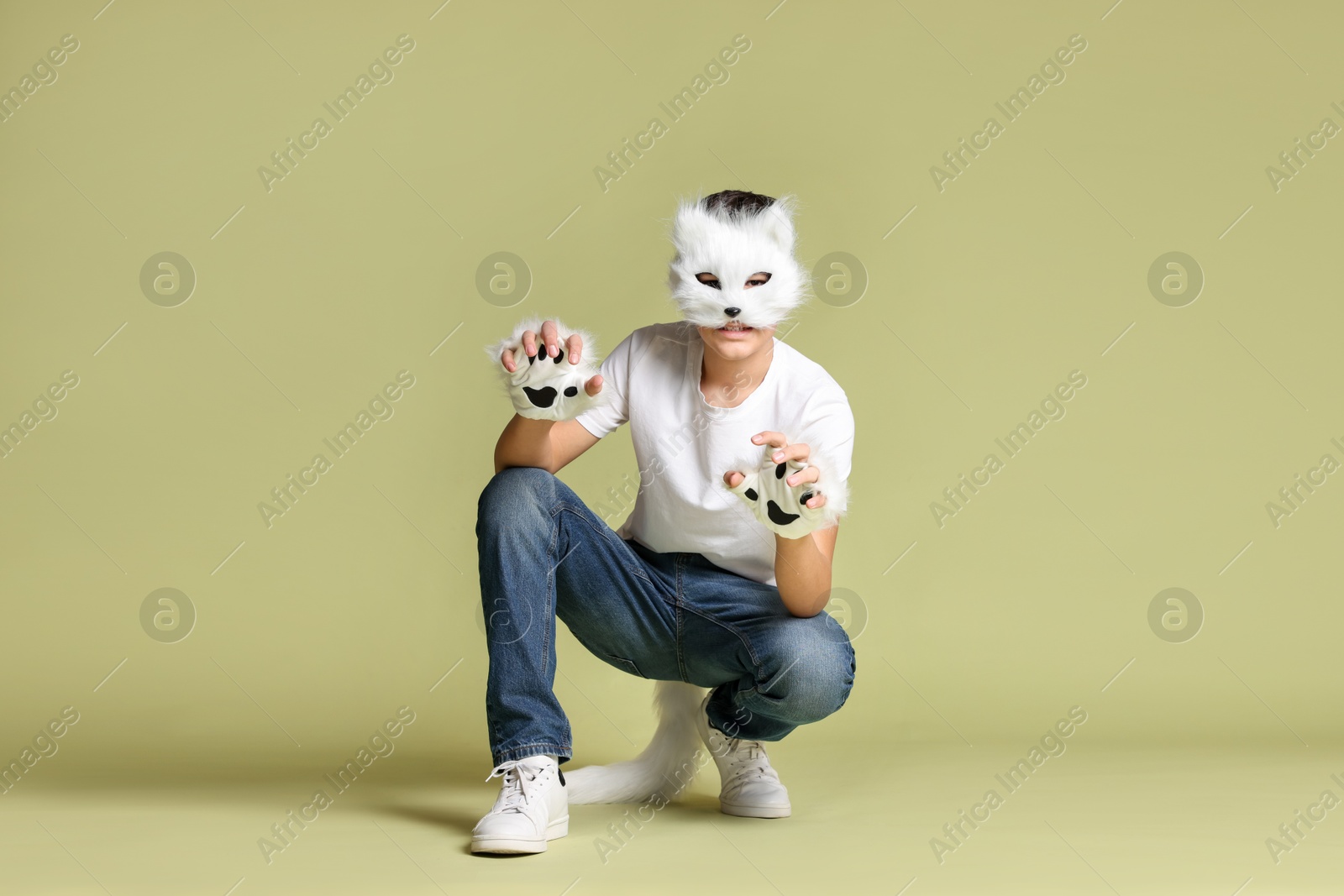 Photo of Quadrobics. Boy wearing cat mask, gloves and tail on pale olive background