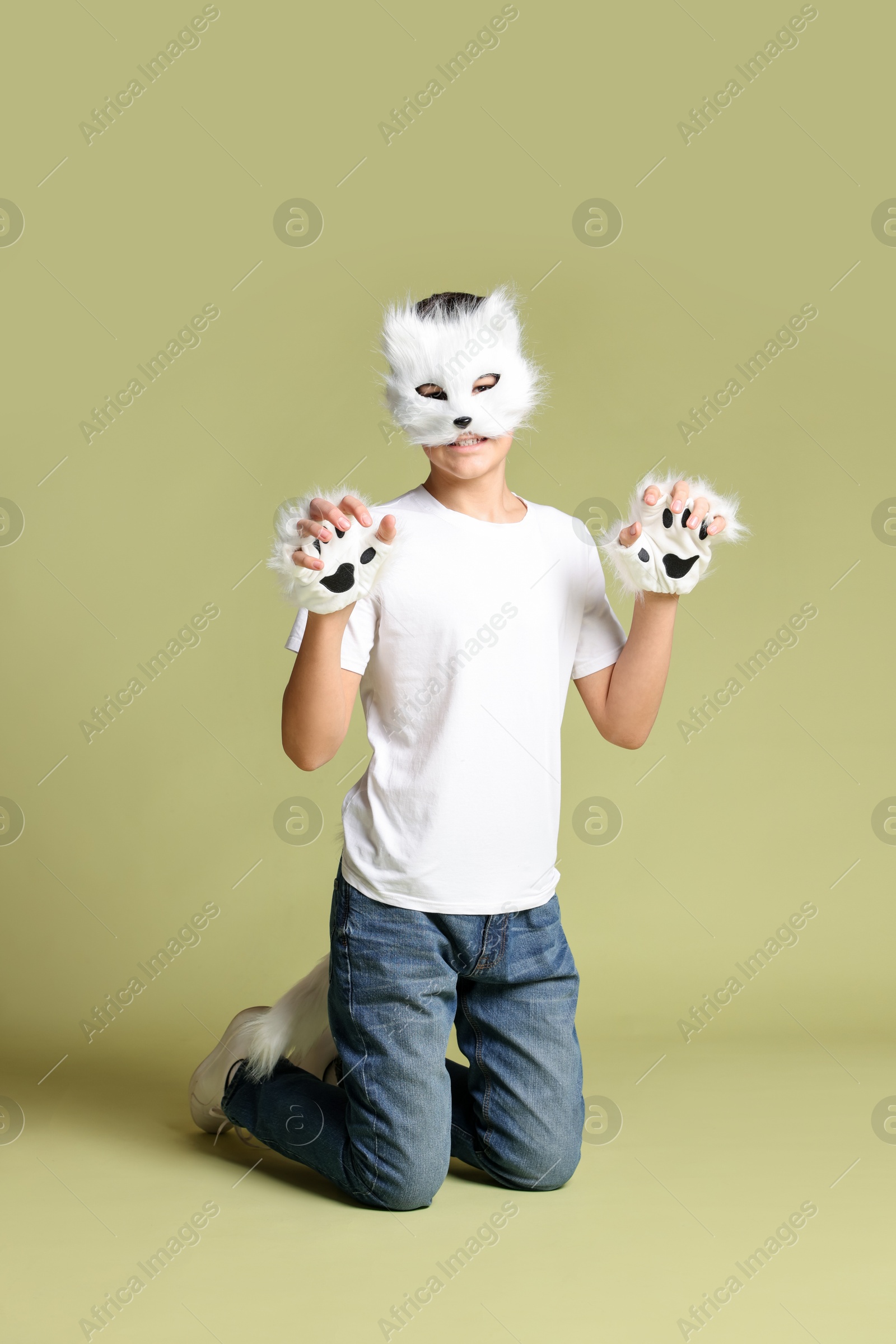 Photo of Quadrobics. Boy wearing cat mask, gloves and tail on pale olive background