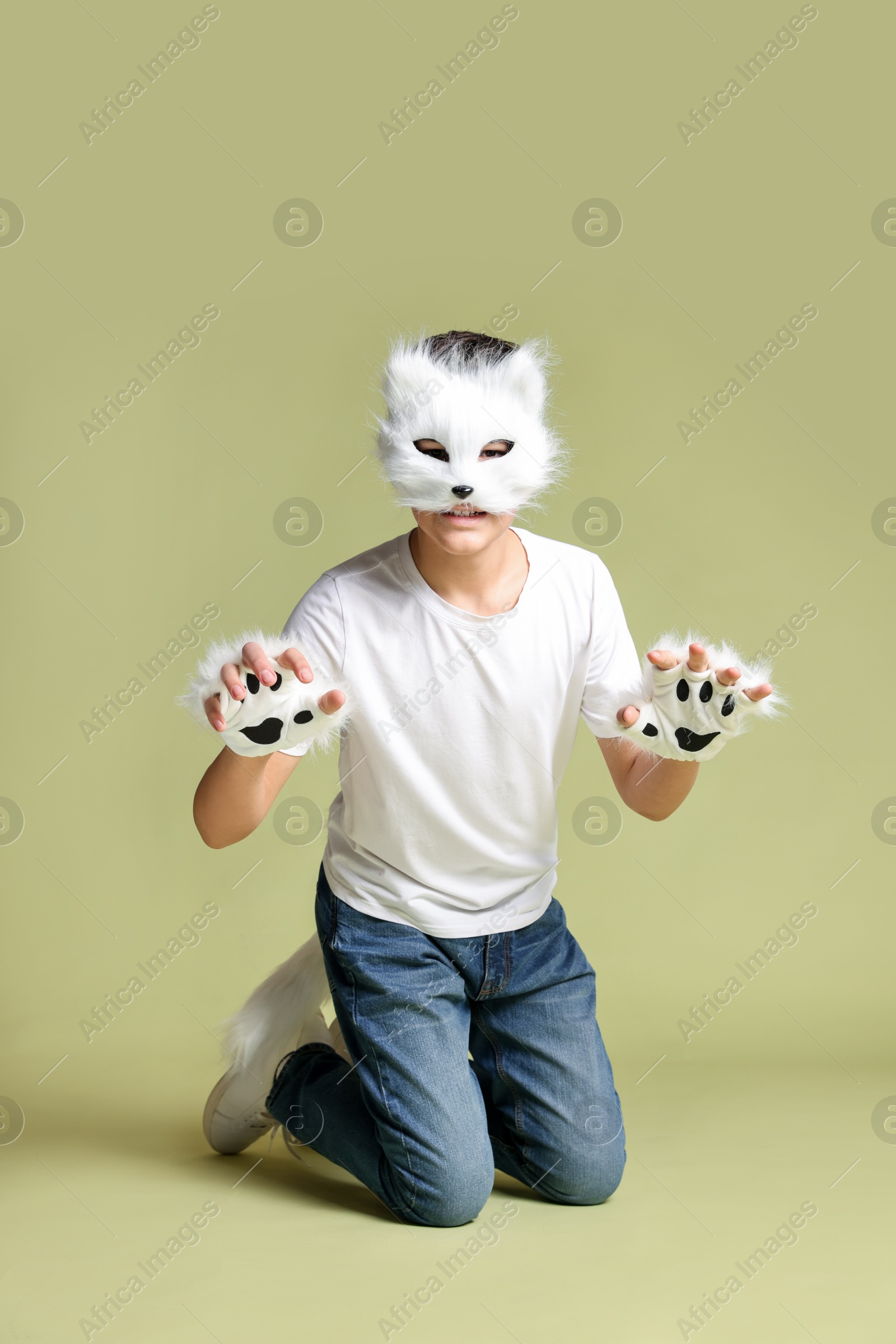 Photo of Quadrobics. Boy wearing cat mask, gloves and tail on pale olive background