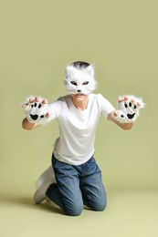 Photo of Quadrobics. Boy wearing cat mask, gloves and tail on pale olive background