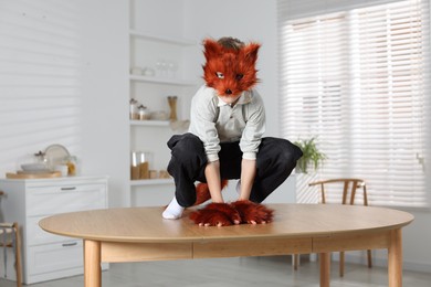 Photo of Quadrobics. Boy wearing fox mask, tail and gloves on table indoors