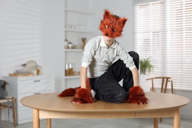 Quadrobics. Boy wearing fox mask, tail and gloves on table indoors