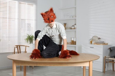 Photo of Quadrobics. Boy wearing fox mask, tail and gloves on table indoors