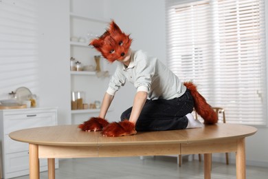 Photo of Quadrobics. Boy wearing fox mask, tail and gloves on table indoors