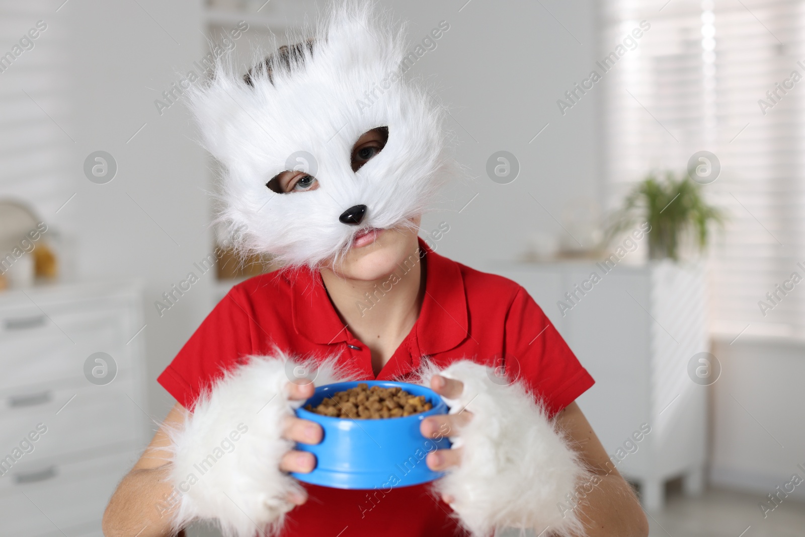 Photo of Quadrobics. Boy wearing cat mask and gloves with feeding bowl indoors