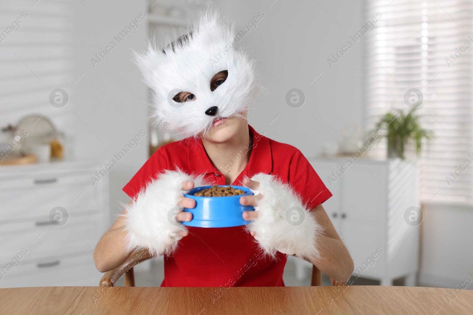 Photo of Quadrobics. Boy wearing cat mask and gloves with feeding bowl at table indoors