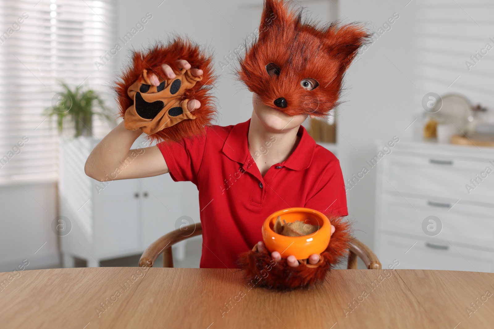 Photo of Quadrobics. Boy wearing fox mask and gloves with feeding bowl at table indoors