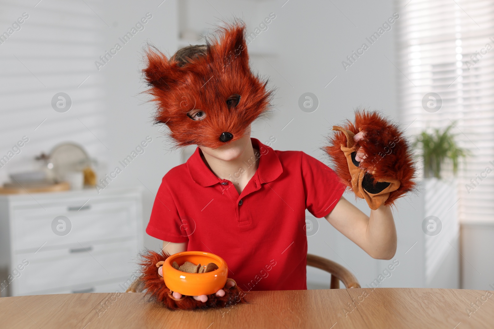 Photo of Quadrobics. Boy wearing fox mask and gloves with feeding bowl at table indoors