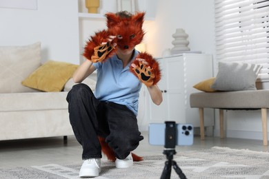 Photo of Quadrobics. Boy wearing fox mask, tail and gloves filming video at home