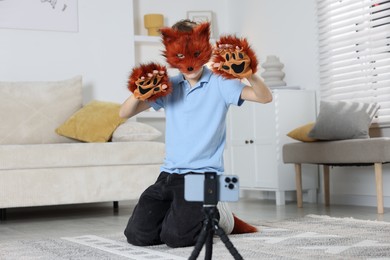 Photo of Quadrobics. Boy wearing fox mask, tail and gloves filming video at home