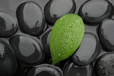 Photo of Spa stones and green leaf on water surface, top view