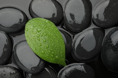 Photo of Spa stones and green leaf on water surface, top view