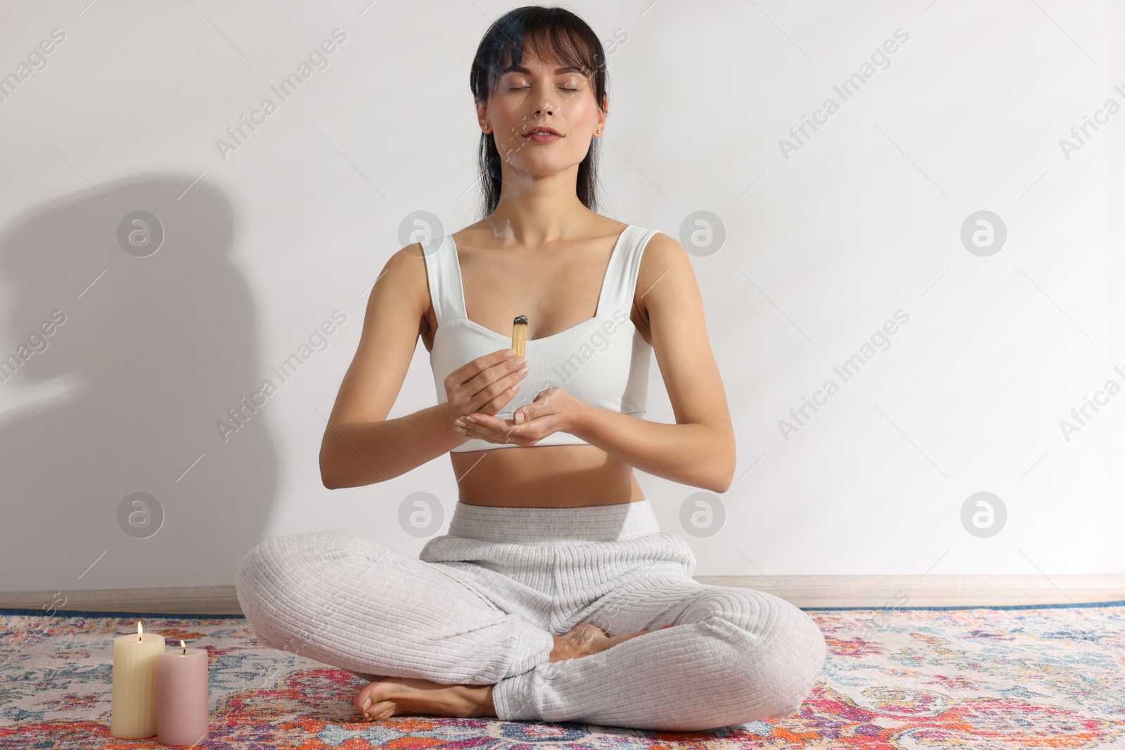 Photo of Woman with smoldering palo santo stick on floor at home