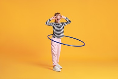 Photo of Cute little girl showing V-signs while exercising with hula hoop on orange background