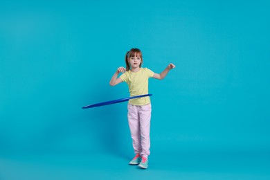 Photo of Cute little girl exercising with hula hoop on light blue background