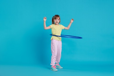 Photo of Cute little girl exercising with hula hoop on light blue background