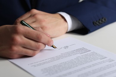 Photo of Man putting signature on document at white table, closeup