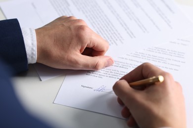 Photo of Man putting signature on document at table, closeup