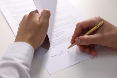 Photo of Man putting signature on document at white table, closeup