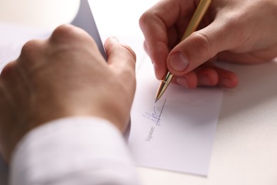 Photo of Man putting signature on document at white table, closeup