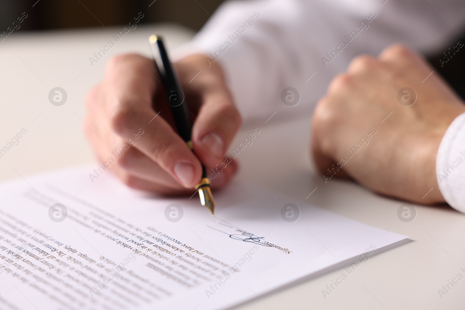 Photo of Man putting signature on document at white table, closeup