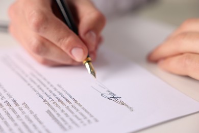 Photo of Man putting signature on document at table, closeup