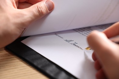 Photo of Man putting signature on document at wooden table, closeup