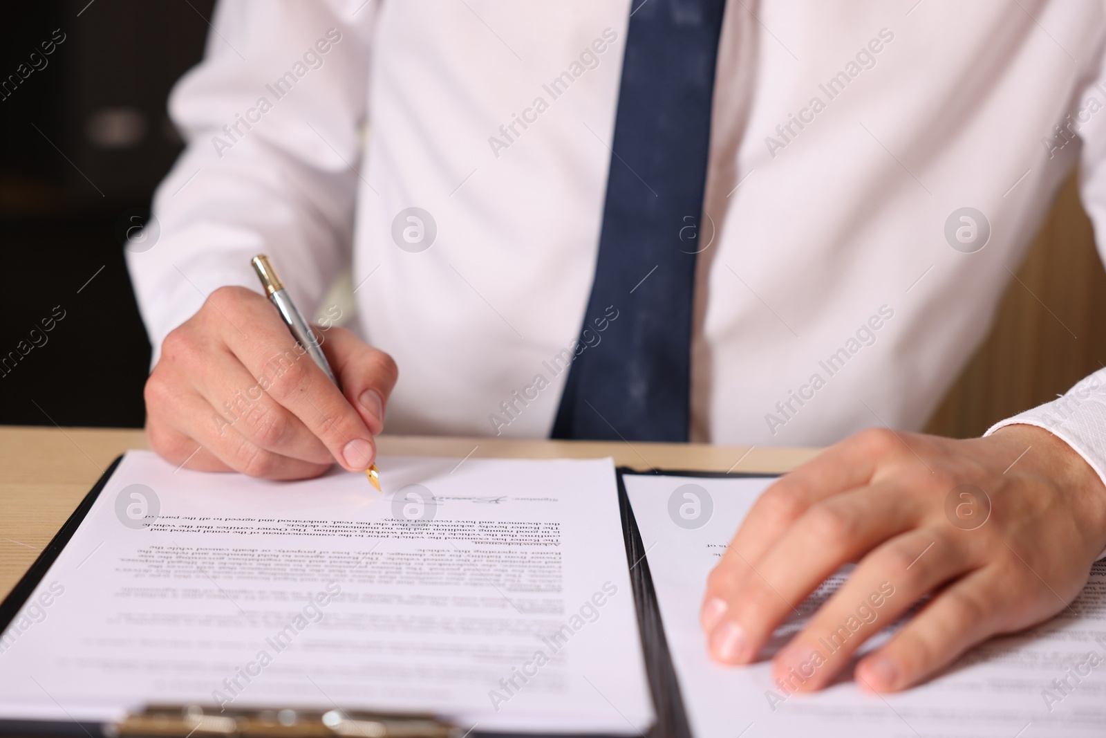 Photo of Man putting signature on document at table, closeup