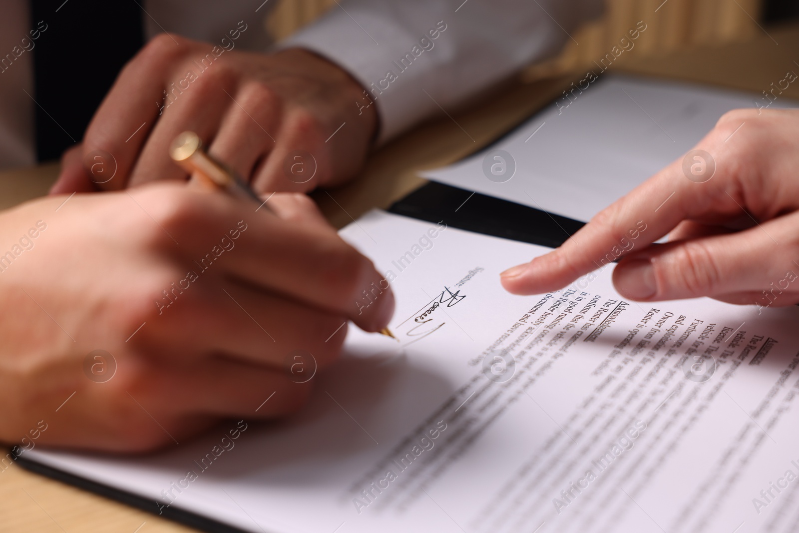 Photo of Woman pointing at document and man putting signature at table, closeup