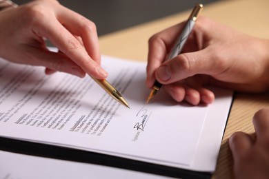 Photo of Woman pointing at document and man putting signature at table, closeup