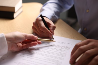 Photo of Woman pointing at document and man putting signature at wooden table, closeup