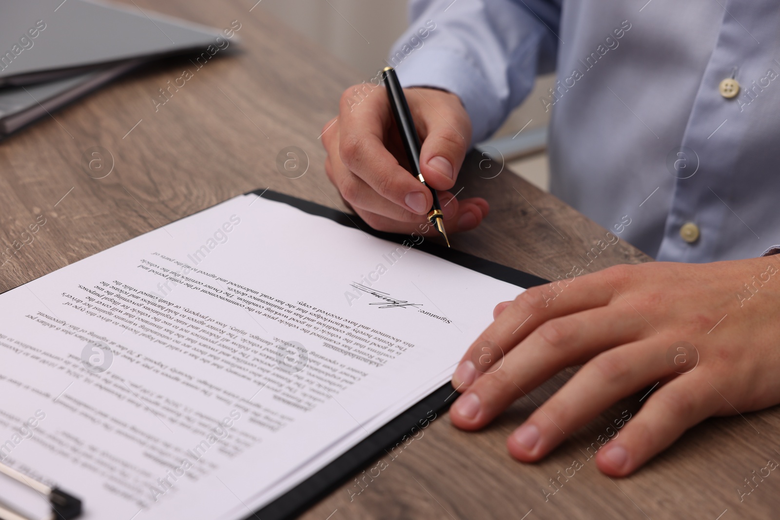 Photo of Man putting signature on document at wooden table, closeup