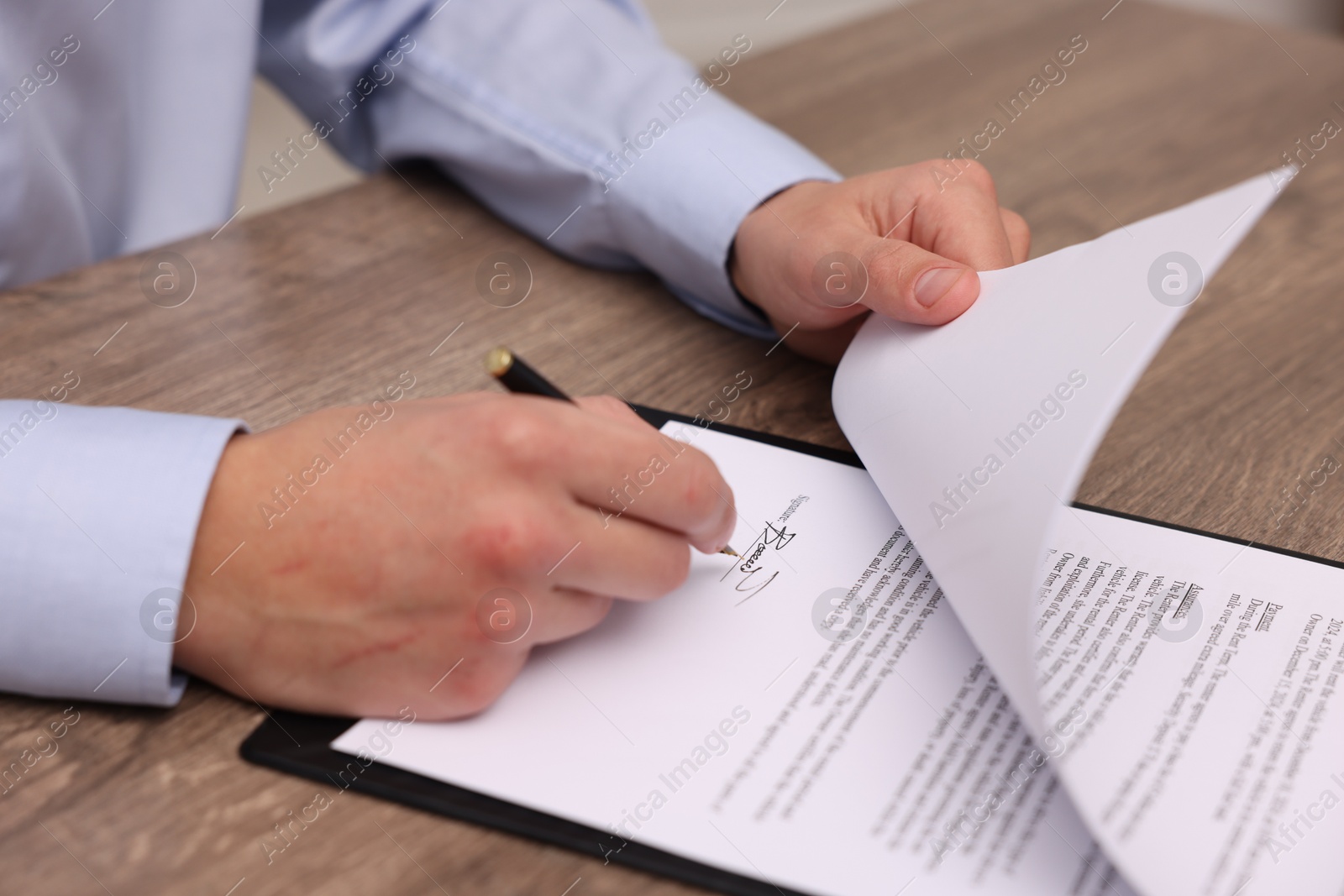 Photo of Man putting signature on document at wooden table, closeup