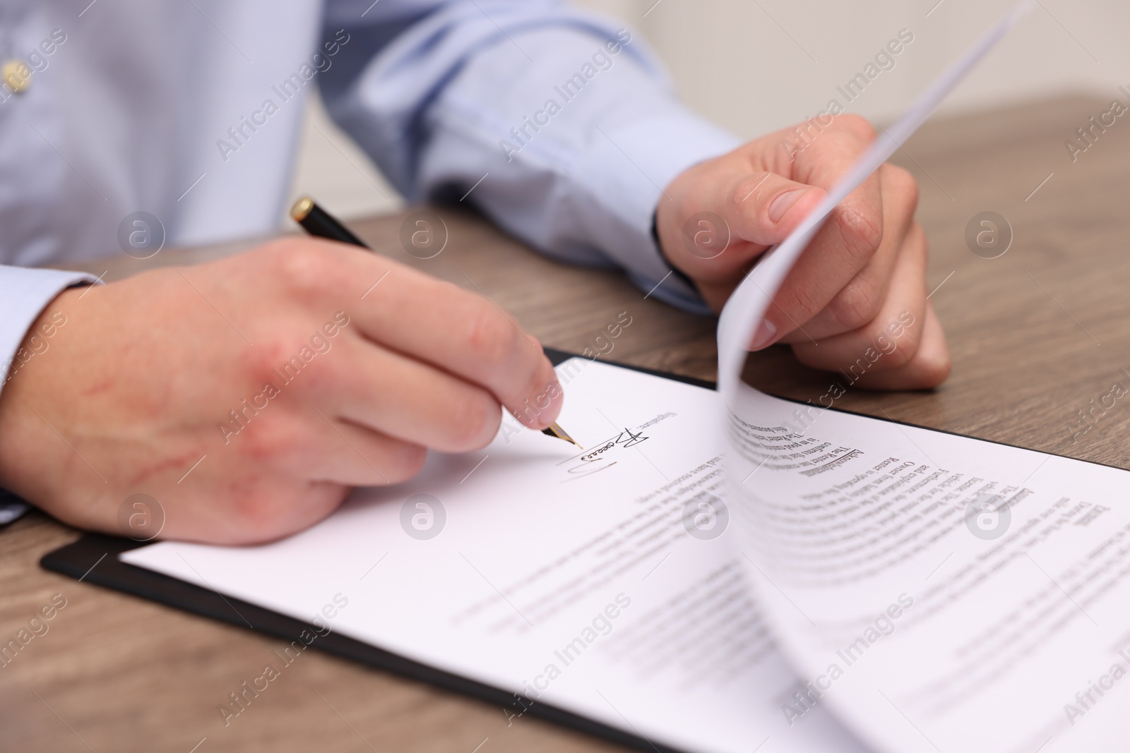 Photo of Man putting signature on document at table, closeup