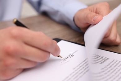 Photo of Man putting signature on document at table, closeup