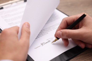 Photo of Man putting signature on document at table, closeup