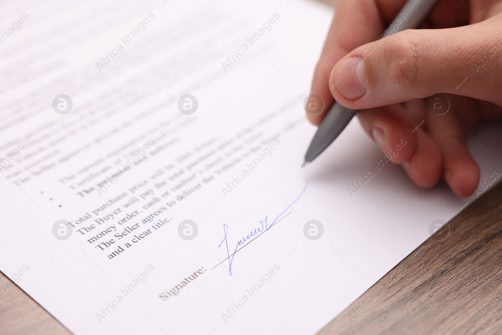 Photo of Man putting signature on document at wooden table, closeup