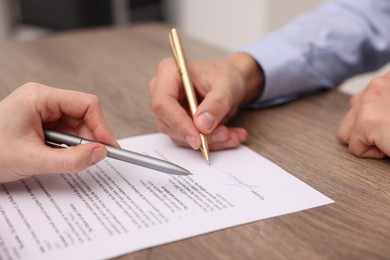 Photo of Woman pointing at document and man putting signature at wooden table, closeup