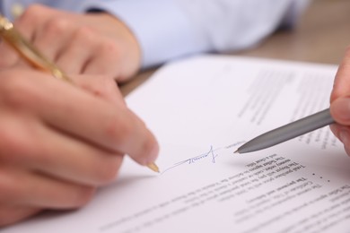 Photo of Woman pointing at document and man putting signature at table, closeup