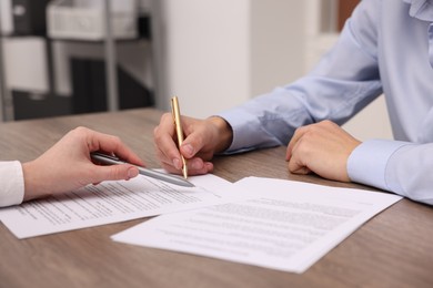 Photo of Woman pointing at document and man putting signature at wooden table, closeup