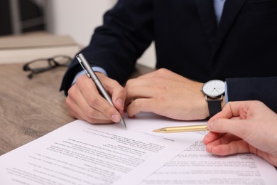 Photo of Woman pointing at document and man putting signature at wooden table, closeup