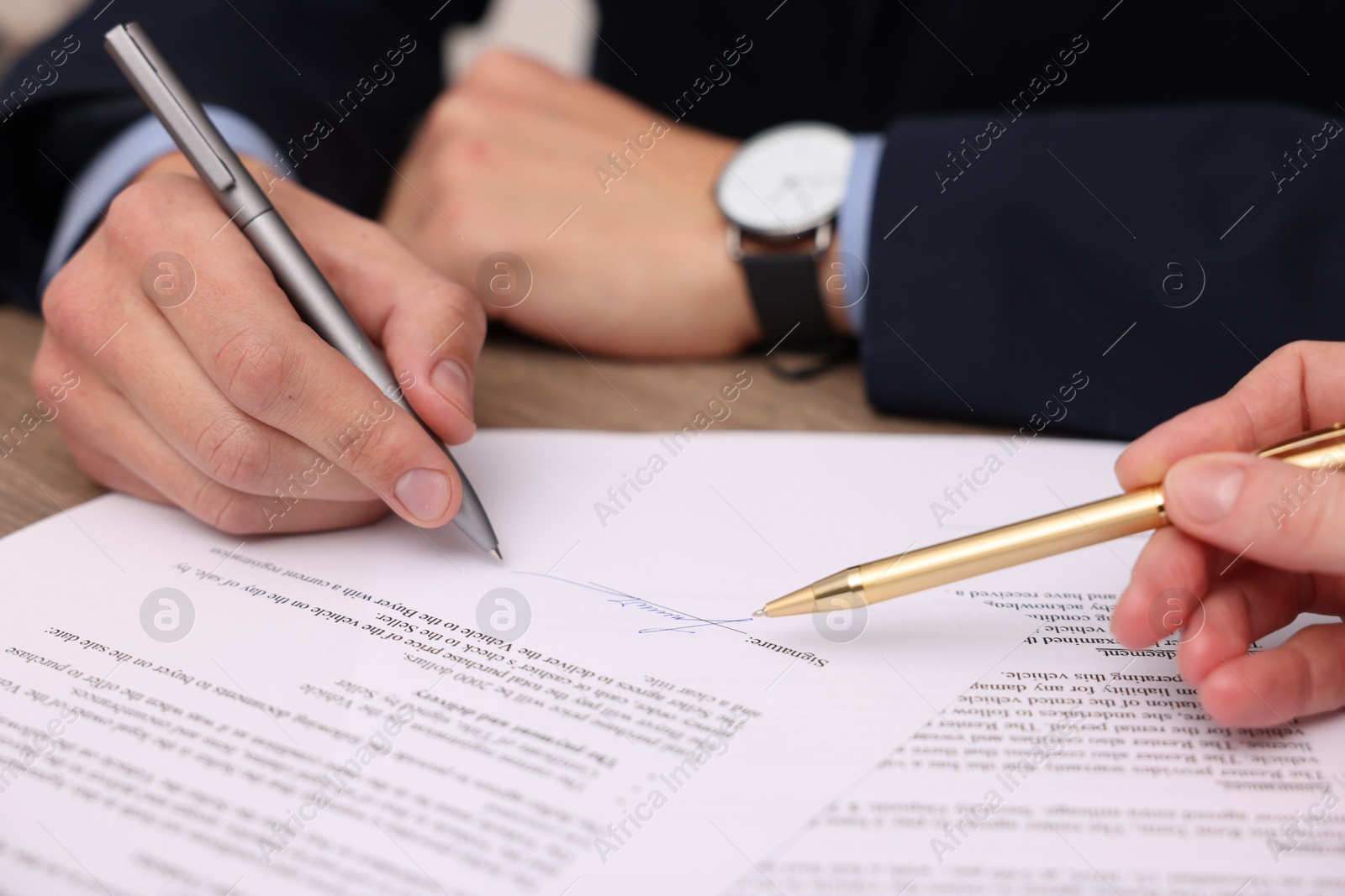 Photo of Woman pointing at document and man putting signature at table, closeup