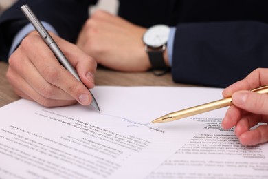 Photo of Woman pointing at document and man putting signature at table, closeup