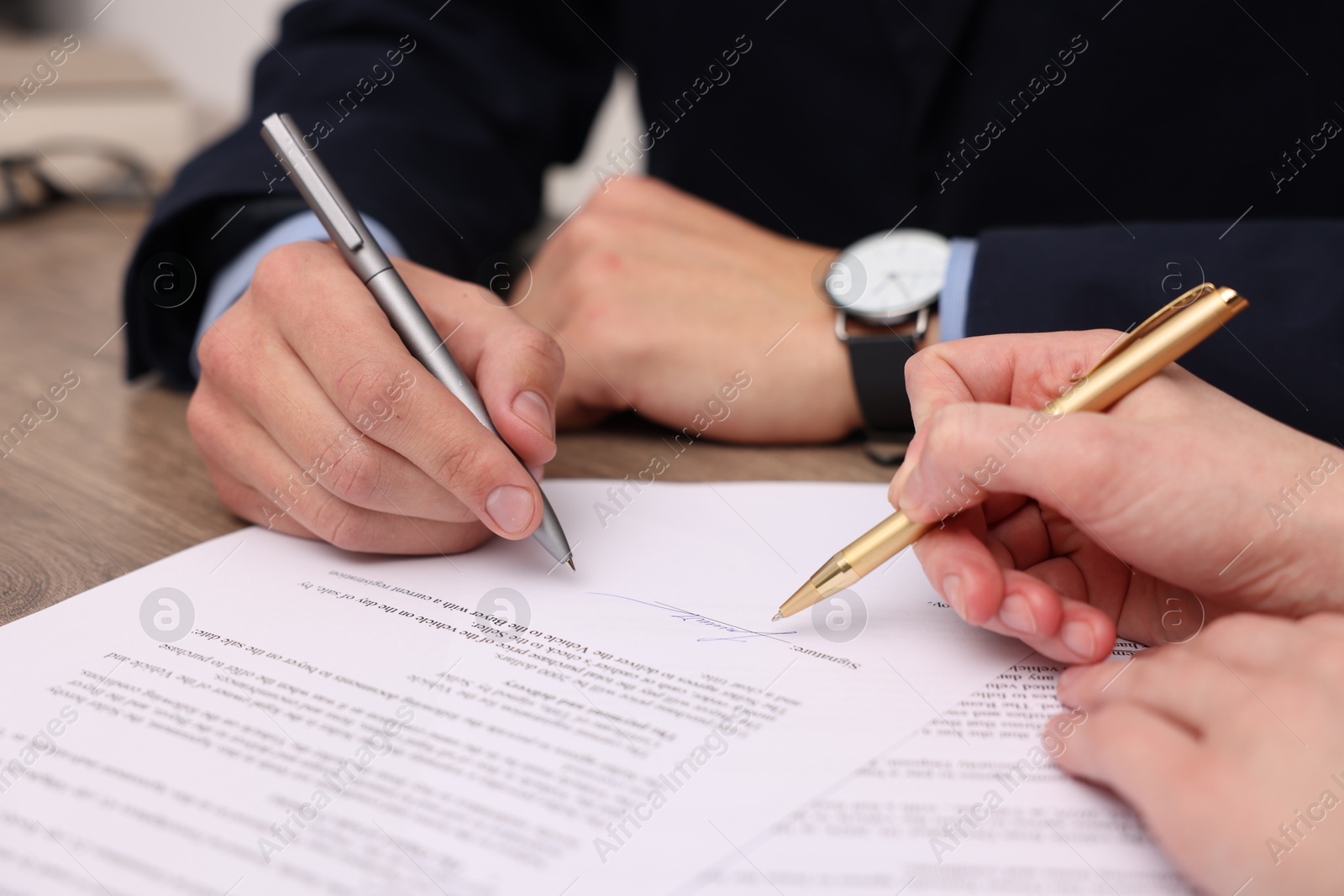 Photo of Woman pointing at document and man putting signature at table, closeup